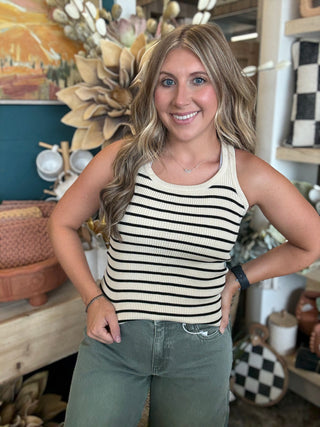 Woman wearing a fitted cream and black striped sleeveless ribbed knit top with olive green pants