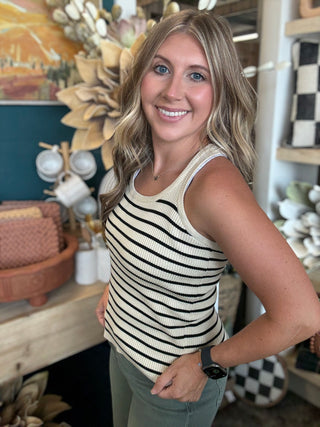 Woman wearing a fitted cream and black striped sleeveless ribbed knit top with olive green pants