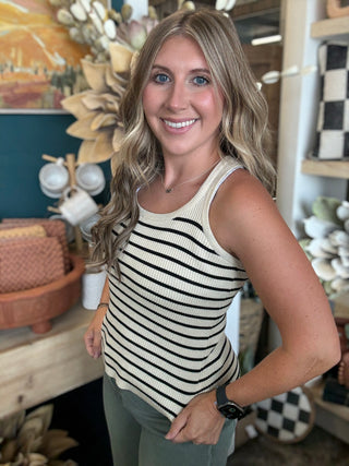 Woman wearing a fitted cream and black striped sleeveless ribbed knit top with olive green pants
