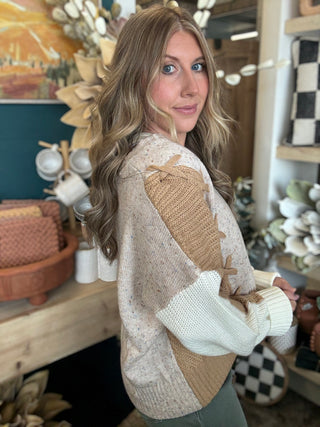 Woman wearing a lace up color block sweater in speckled oatmeal, camel and ivory.
