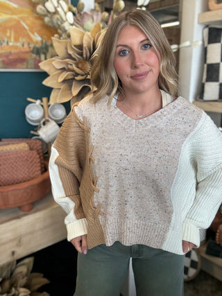 Woman wearing a lace up color block sweater in speckled oatmeal, camel and ivory.