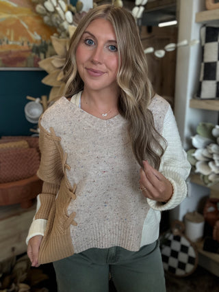 Woman wearing a lace up color block sweater in speckled oatmeal, camel and ivory.