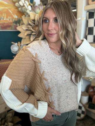 Woman wearing a lace up color block sweater in speckled oatmeal, camel and ivory.