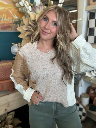 Woman wearing a lace up color block sweater in speckled oatmeal, camel and ivory.