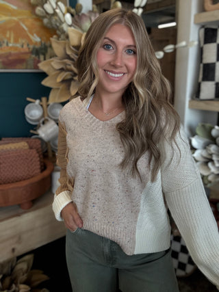 Woman wearing a lace up color block sweater in speckled oatmeal, camel and ivory.
