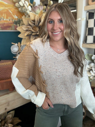 Woman wearing a lace up color block sweater in speckled oatmeal, camel and ivory.