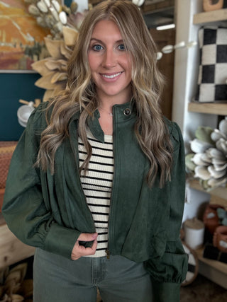 Woman wearing a forest green gathered blouson jacket with high collar, zip front and puff sleeve detailing.