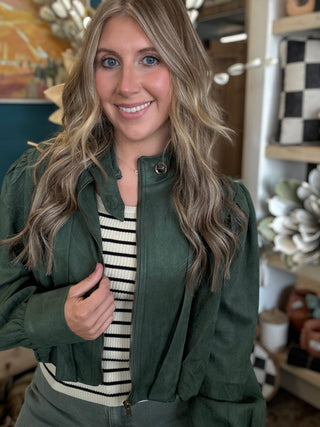 Woman wearing a forest green gathered blouson jacket with high collar, zip front and puff sleeve detailing.
