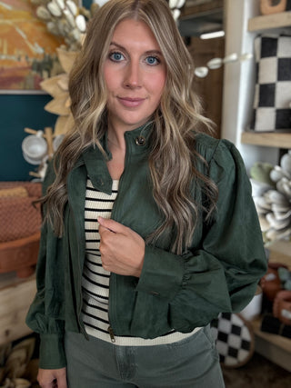 Woman wearing a forest green gathered blouson jacket with high collar, zip front and puff sleeve detailing.