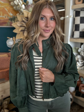 Woman wearing a forest green gathered blouson jacket with high collar, zip front and puff sleeve detailing.