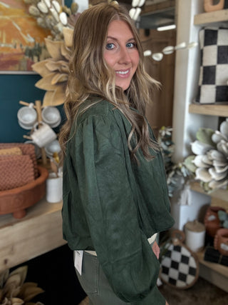 Woman wearing a forest green gathered blouson jacket with high collar, zip front and puff sleeve detailing.