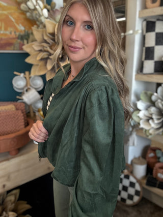 Woman wearing a forest green gathered blouson jacket with high collar, zip front and puff sleeve detailing.
