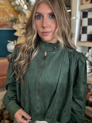 Woman wearing a forest green gathered blouson jacket with high collar, zip front and puff sleeve detailing.