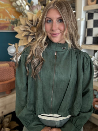 Woman wearing a forest green gathered blouson jacket with high collar, zip front and puff sleeve detailing.