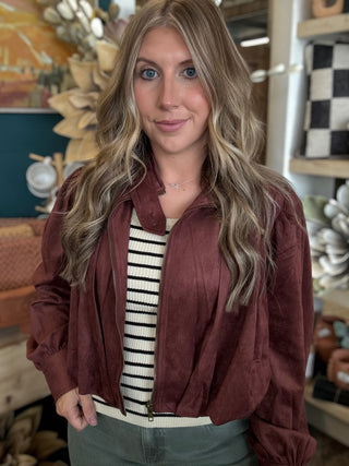 Woman wearing a burgundy gathered blouson jacket with zip front, high neckline and puff sleeves.