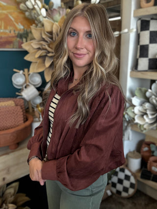 Woman wearing a burgundy gathered blouson jacket with zip front, high neckline and puff sleeves.