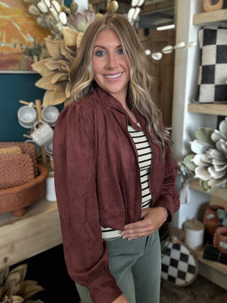 Woman wearing a burgundy gathered blouson jacket with zip front, high neckline and puff sleeves.
