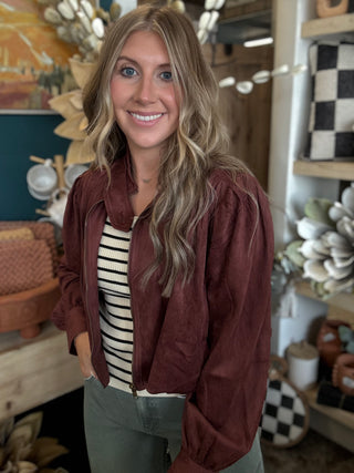 Woman wearing a burgundy gathered blouson jacket with zip front, high neckline and puff sleeves.