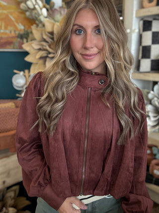 Woman wearing a burgundy gathered blouson jacket with zip front, high neckline and puff sleeves.