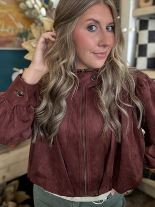 Woman wearing a burgundy gathered blouson jacket with zip front, high neckline and puff sleeves.