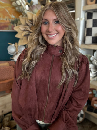 Woman wearing a burgundy gathered blouson jacket with zip front, high neckline and puff sleeves.