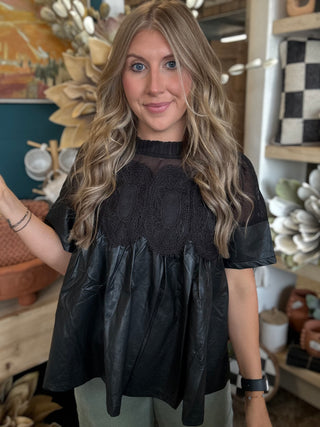 Woman wearing a black lace overlay faux leather babydoll top with sheer mesh neckline and short sleeves.