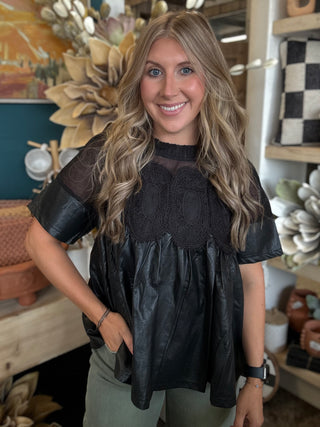 Woman wearing a black lace overlay faux leather babydoll top with sheer mesh neckline and short sleeves.