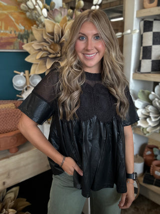 Woman wearing a black lace overlay faux leather babydoll top with sheer mesh neckline and short sleeves.