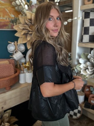 Woman wearing a black lace overlay faux leather babydoll top with sheer mesh neckline and short sleeves.