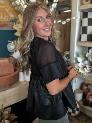 Woman wearing a black lace overlay faux leather babydoll top with sheer mesh neckline and short sleeves.