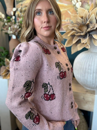 Woman wearing a dusty-pink cherry motif button-front cardigan from Pill Box Boutique