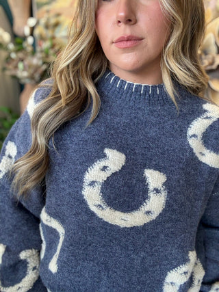A close-up of a woman wearing a navy blue knit sweater with large white horseshoe patterns, cropped from the nose down.