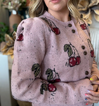 Woman wearing a dusty-pink cherry motif button-front cardigan from Pill Box Boutique
